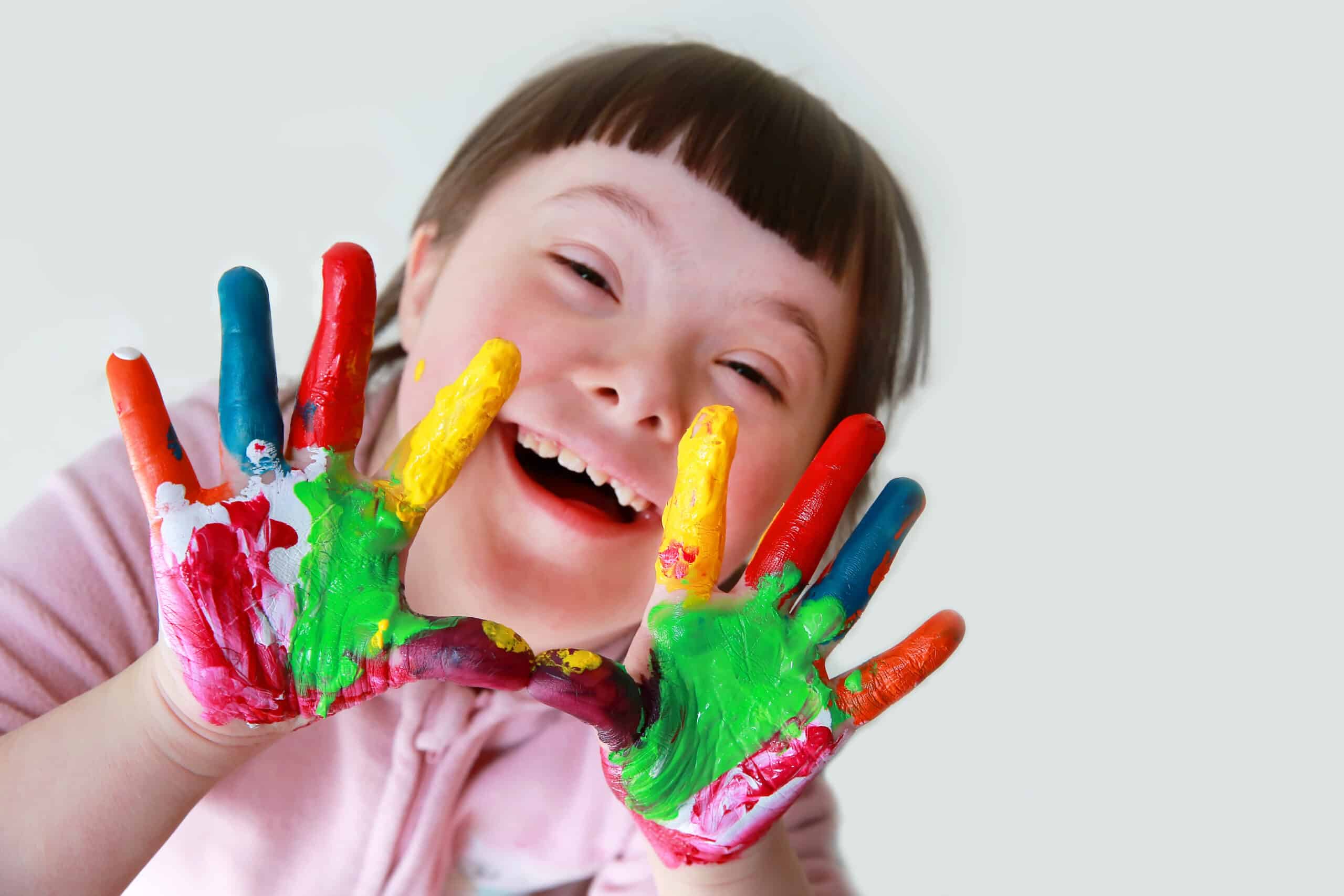 Glad jente med Downs syndrom som har mange ulike farger malt på hendene.