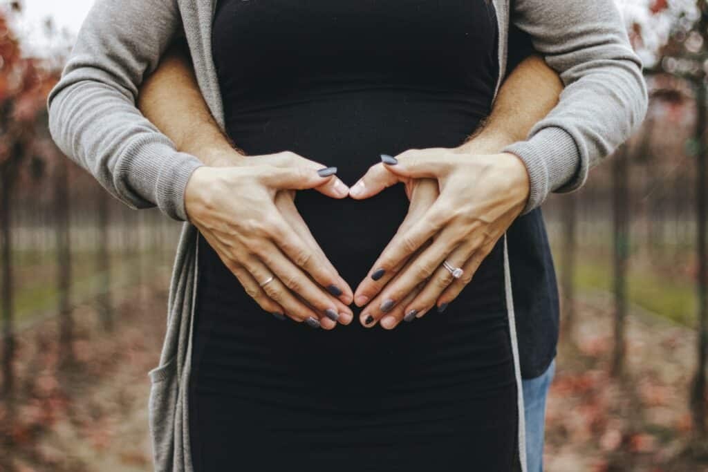 Et par som former hjerter med hendene foran en gravid mage