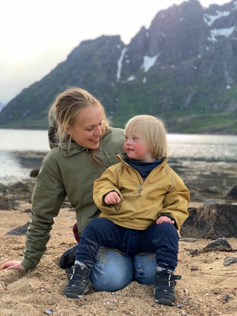mor sitter på strand med sønn med downs syndrom