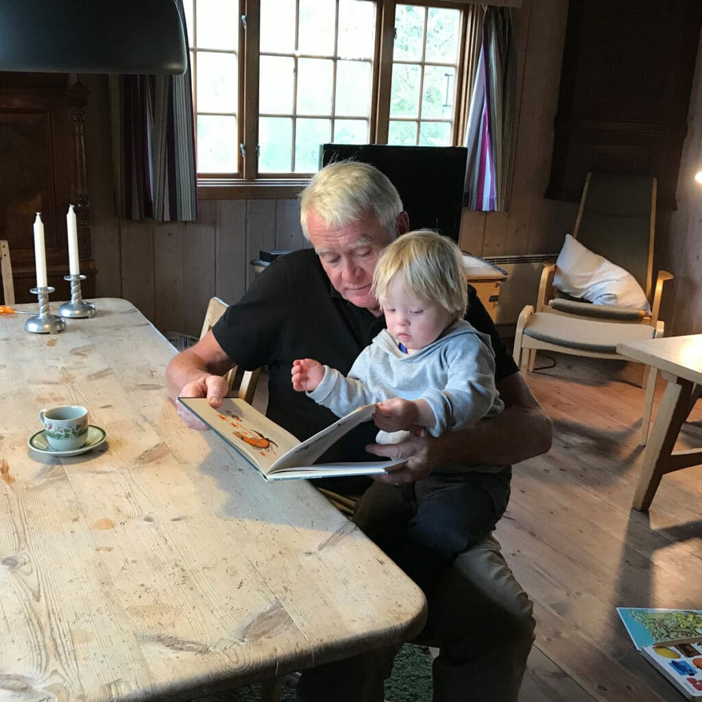 Tollef sitter på fanget til bestefar og leser i bok