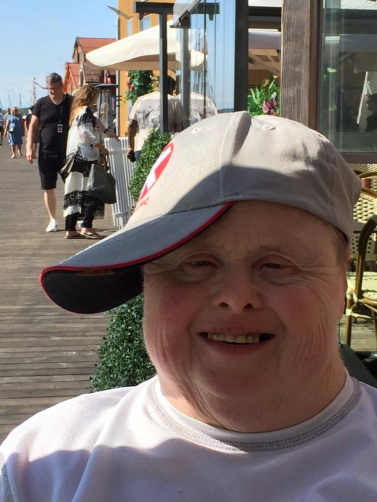 eldre kvinne med downs syndrom smiler til kamera. hun har caps på sidelengs