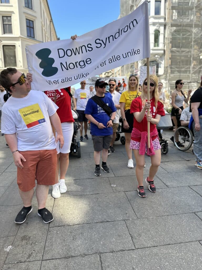 Mennesker med og uten Downs syndrom går i parade med parolen "Vi er alle ulike - vi er alle unike."