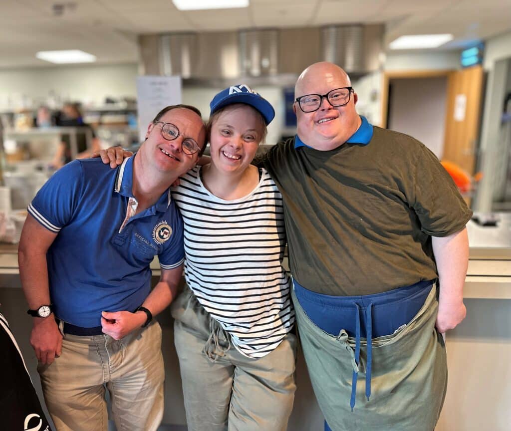 Tre voksne mennesker med Downs syndrom som holder rundt hverandre og smiler
