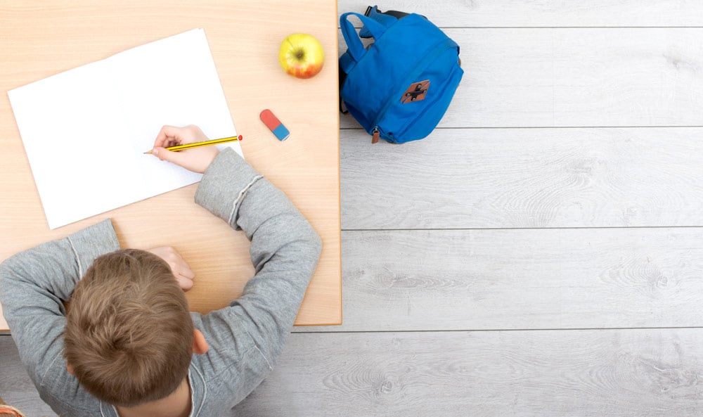 elev som skriver på blank side, med eple og viskelær på pulten og sekk på gulvet