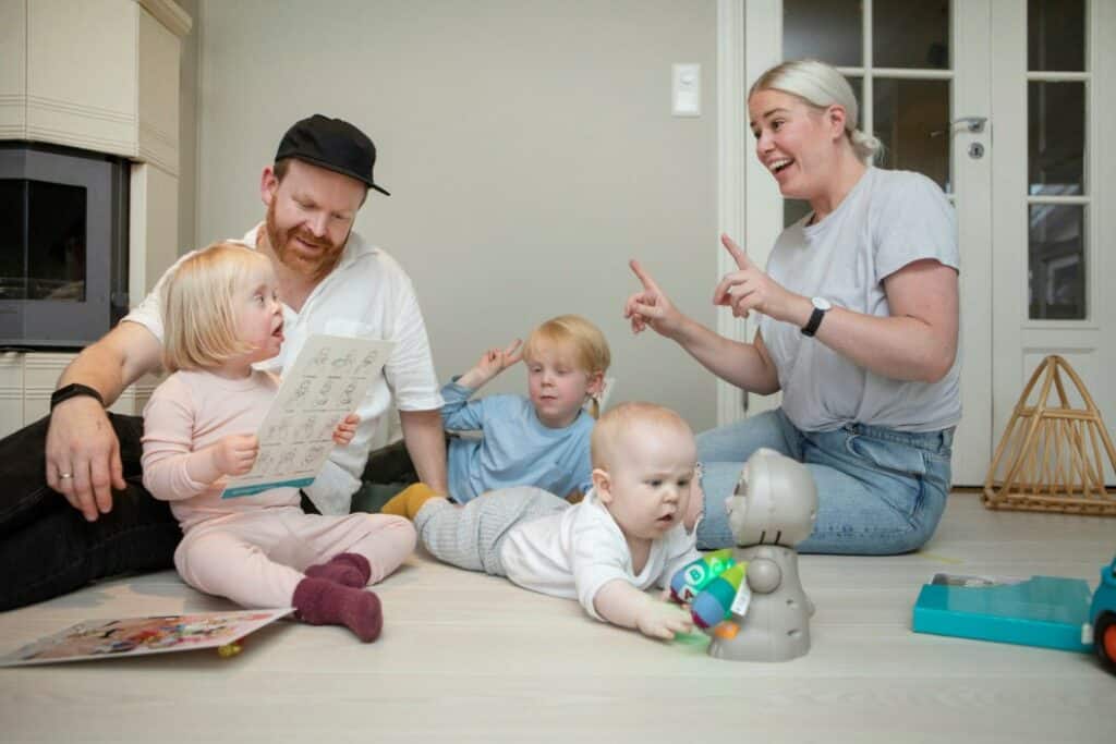 Familie med to voksne og tre barn som sitter på gulvet sammen