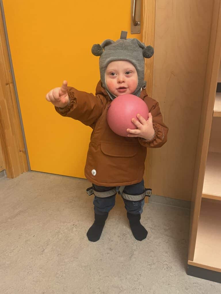 Liten gutt ed Downs syndrom som peker og holder en ball