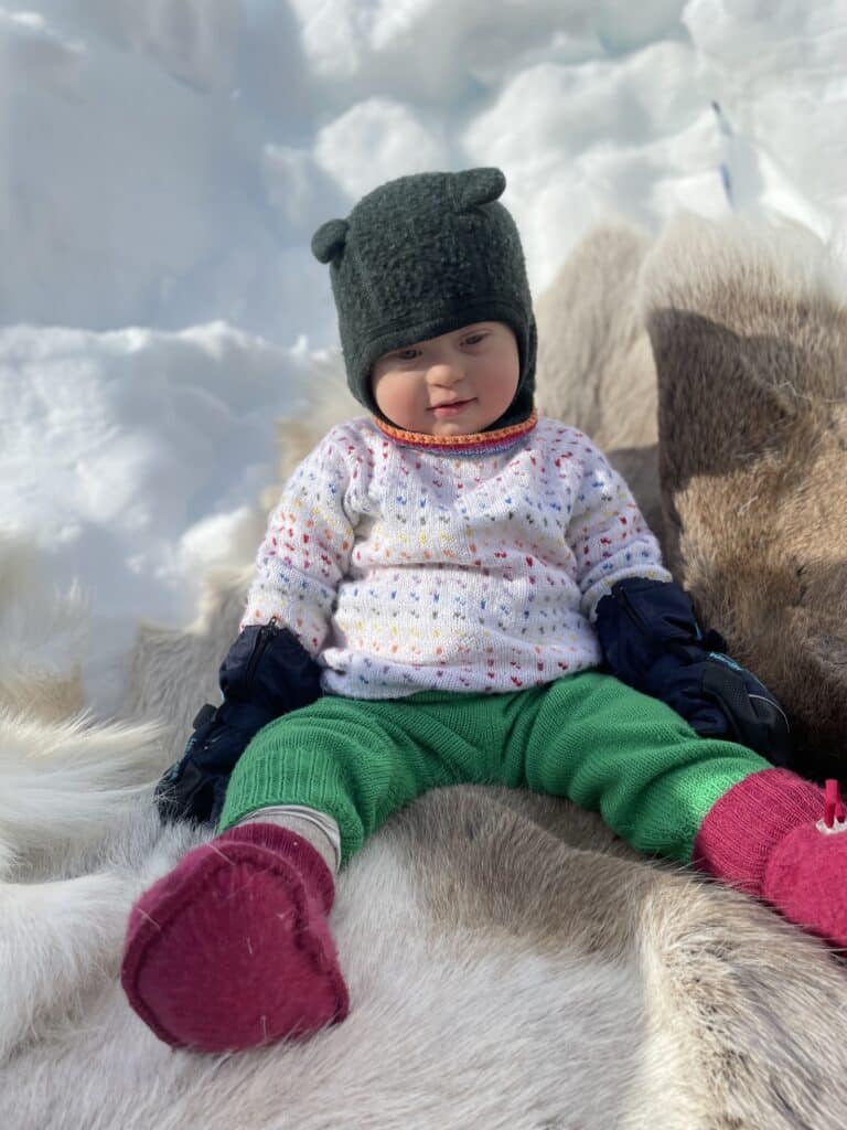 Liten gutt med Downs syndrom sitter på reinsdyrskinn i snøen