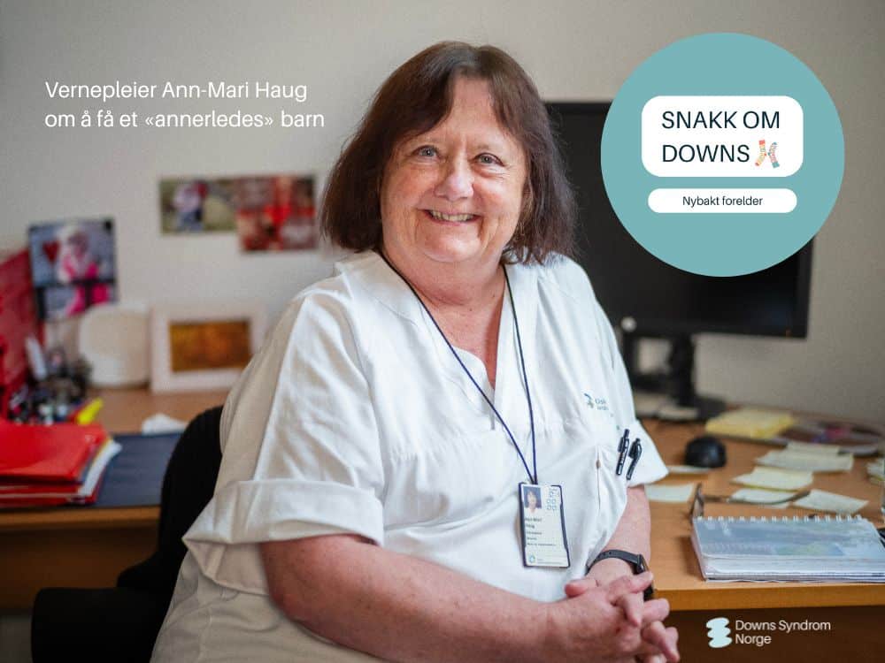 Eldre kvinne som sitter foran kontorpult og smiler til kamera