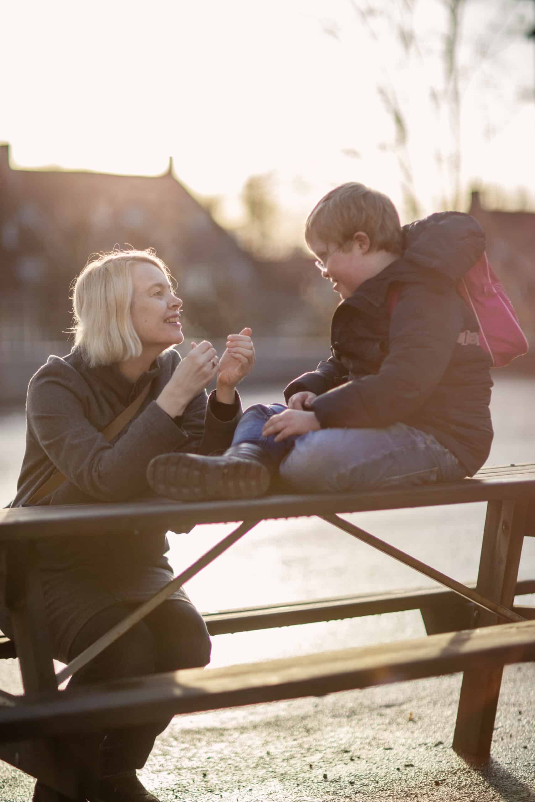 Mor og sønn med Downs syndrom sitter på benk og kommuniserer med hendene