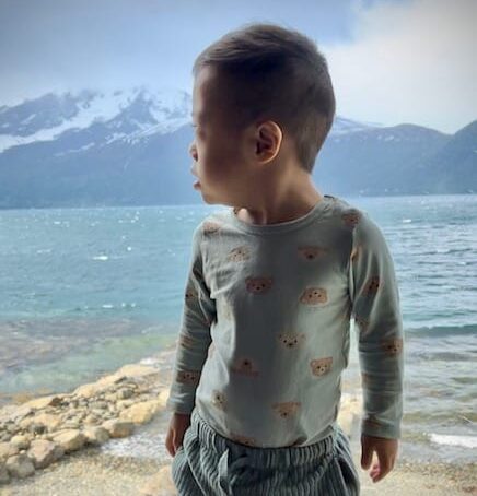 En liten gutt som ser utover en fjord med fjell i bakgrunnen