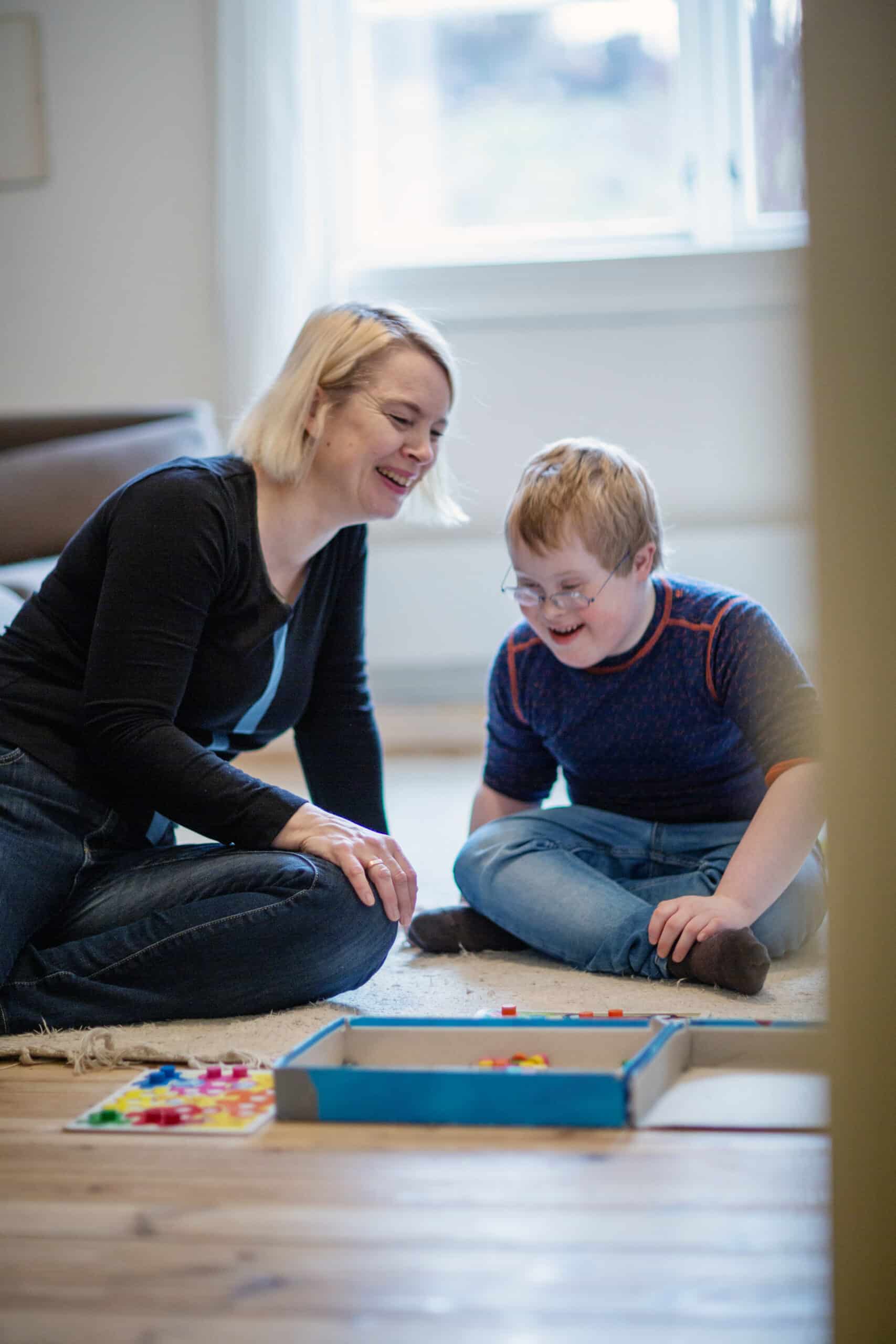 Mor og sønn med Downs syndrom sitter på gulvet og ler og spiller spill