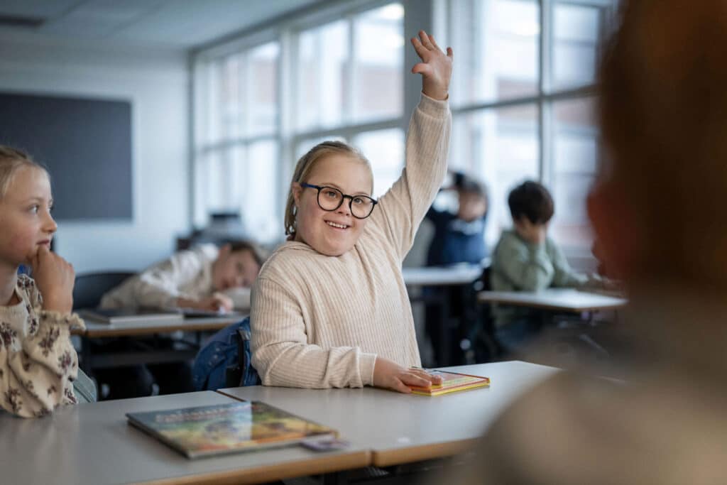 Jente med Downs syndrom som rekker opp hånda i klasserommet
