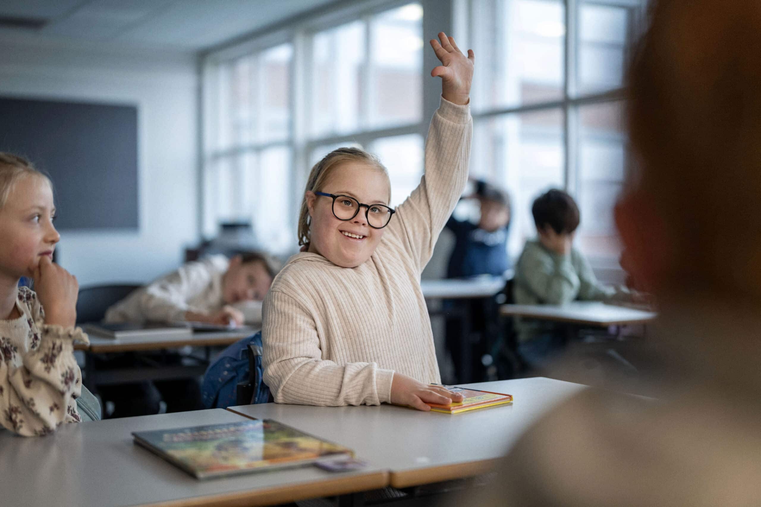 Jente med Downs syndrom som rekker opp hånda i klasserommet