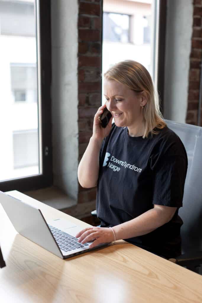 Dame som sitter forran PC og snakker i telefon