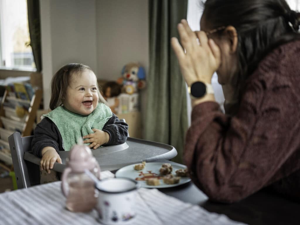 Lite barn med Downs syndrom som spiser og ler av mor som tuller
