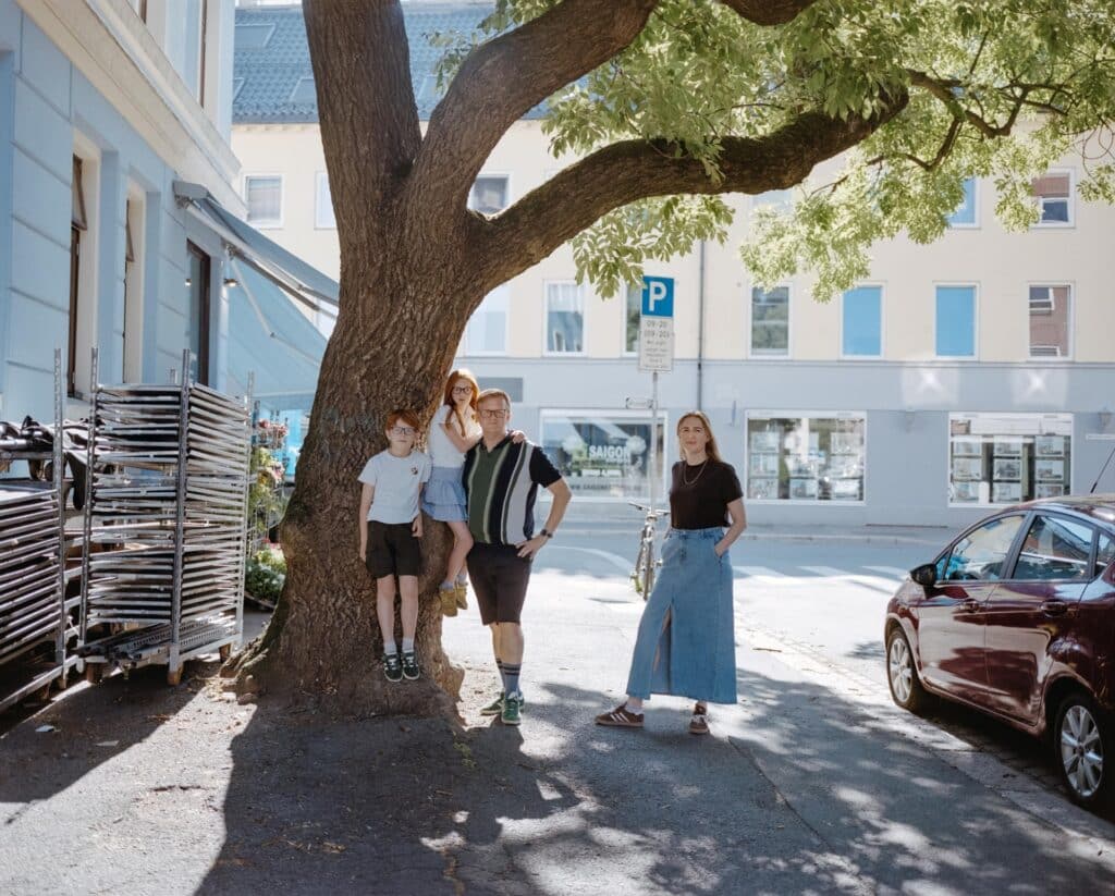 Familie med to voksne og to barn som står ved et stort tre i en bygate. Et av barna har Downs syndrom.