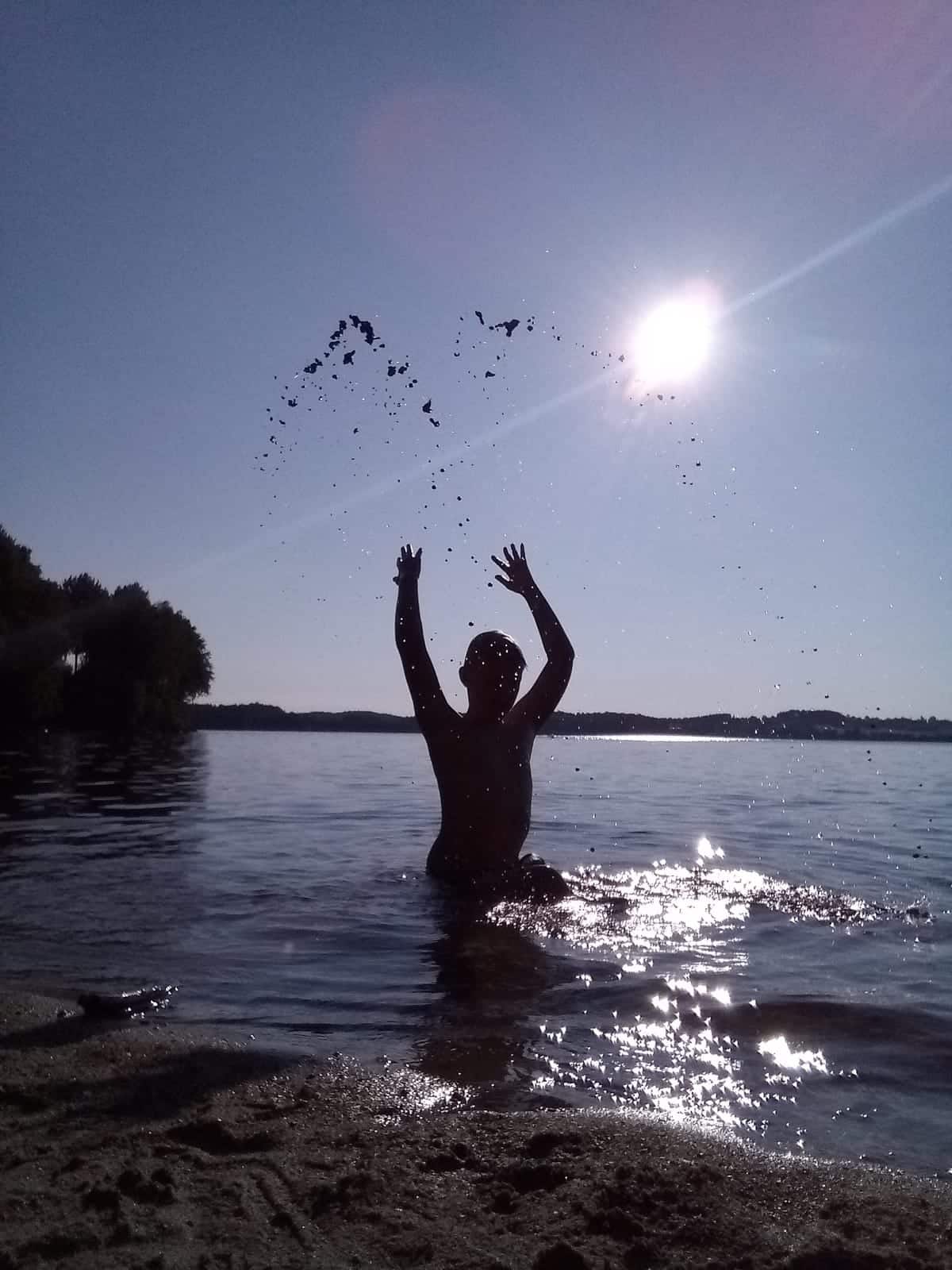 Barn som leker i vannet og kaster sand over hodet